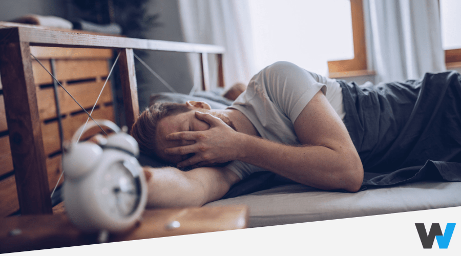 man lying on bed covering face with hand