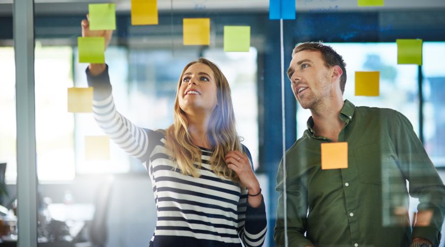 two young professionals looking at sticky notes on a window