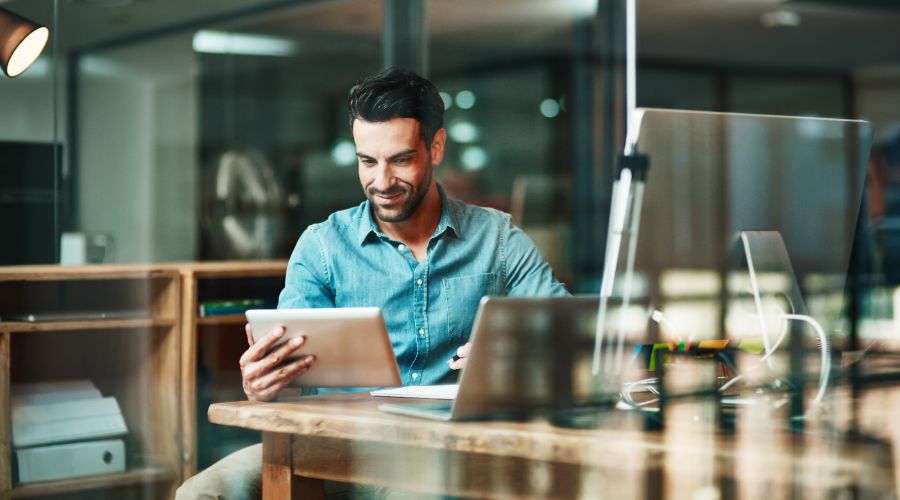 man looking at tablet with computer and laptop on desk