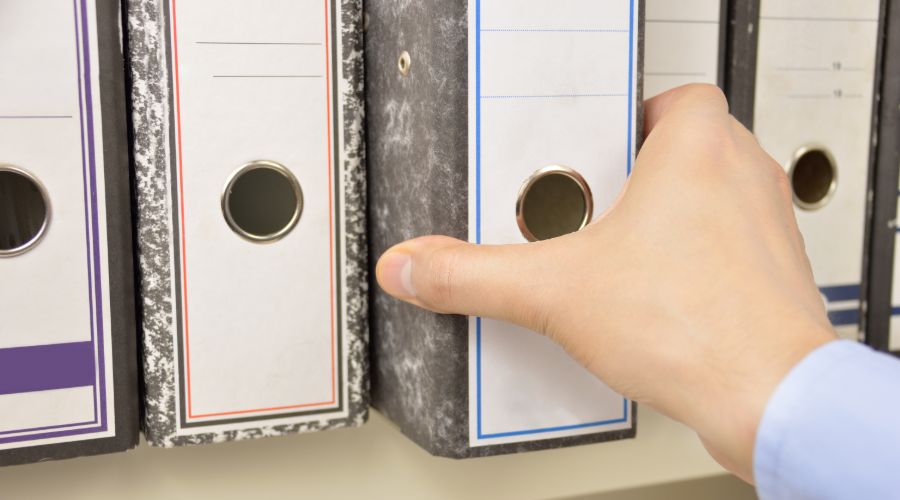 man's hand pulling out a binder from a shelf