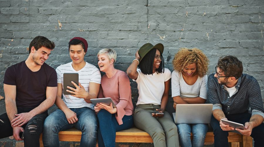 group of millennials laughing and looking at phones, tablets, and computers