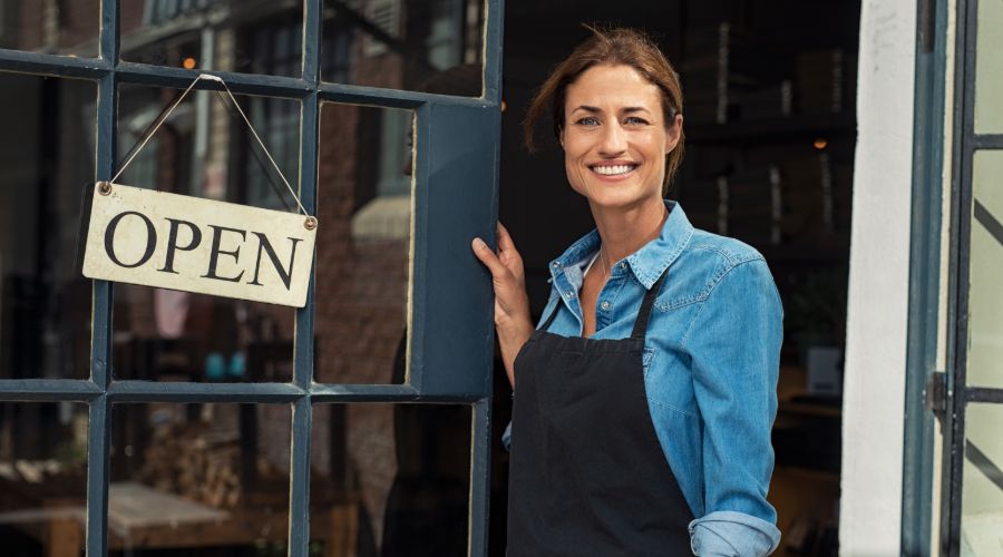 Small business owner standing in front of her store with an open sign