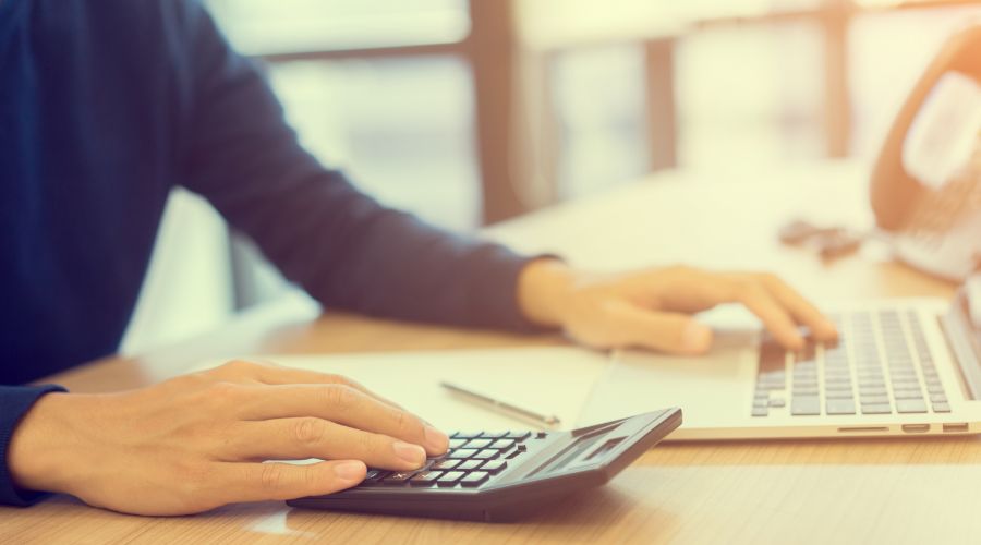 person using a calculator and laptop to determine an employee's net pay