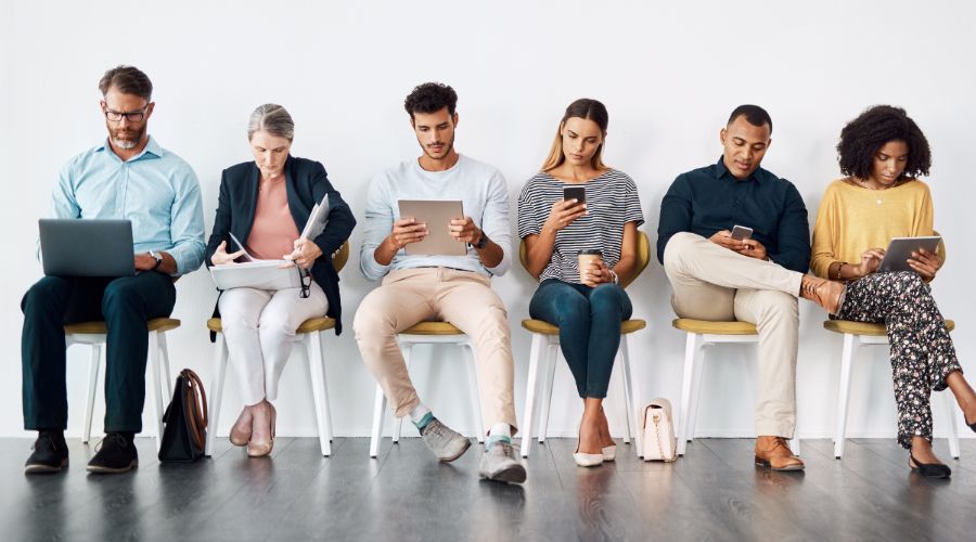 A group of employees and independent contractors looks at their laptops, phones, tablets, and paperwork