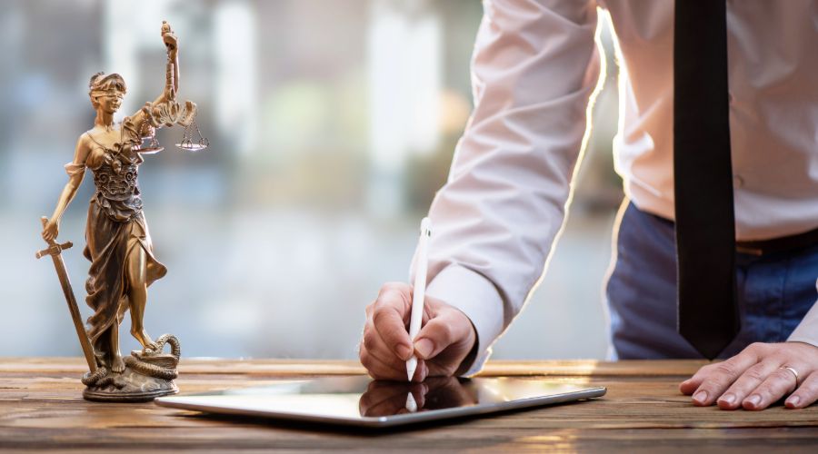 attorney using a tablet and stylus to review payroll with a figurine of Lady Justice